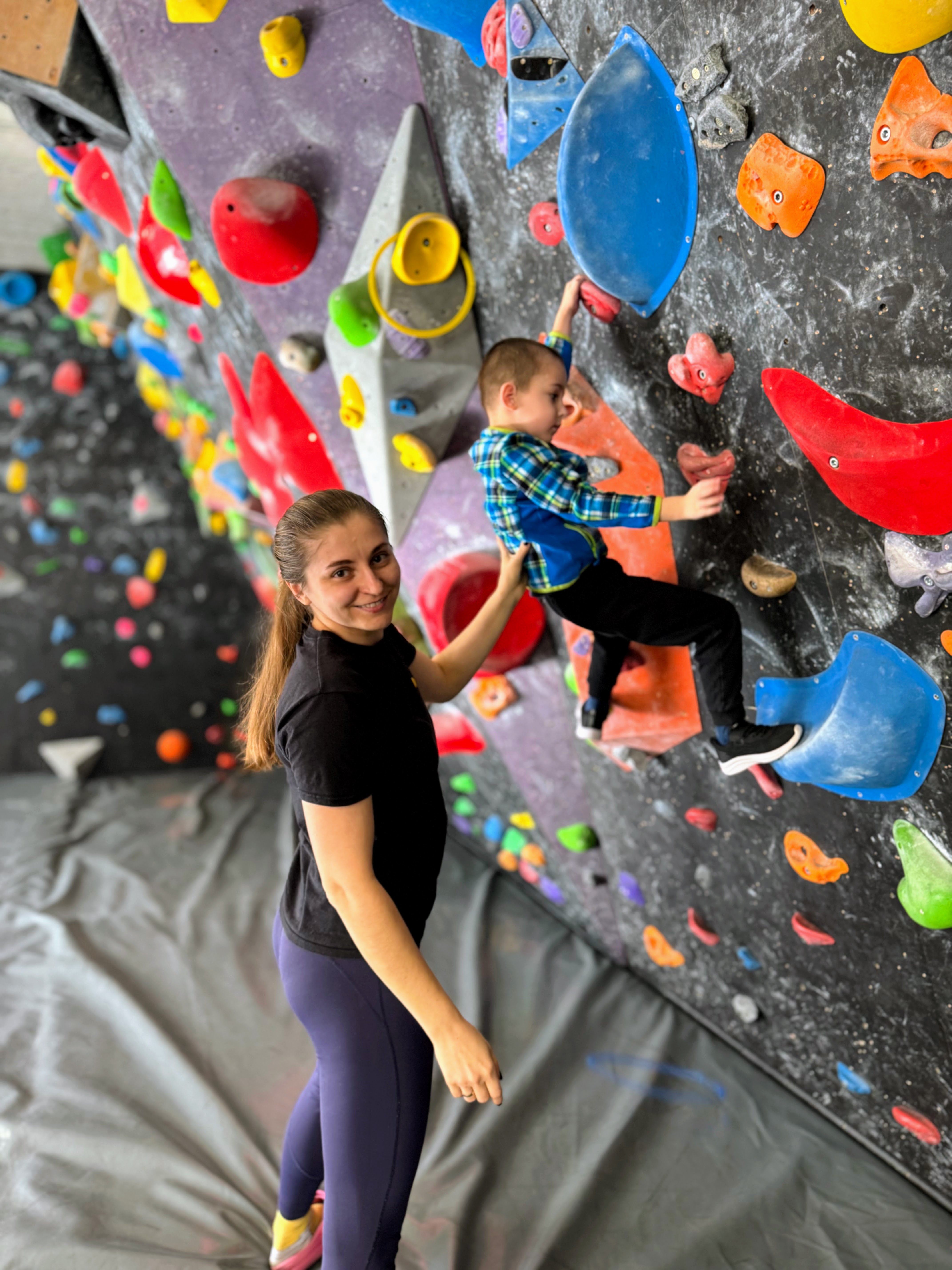 Coach guiding child safely on climbing wall with crash mats below